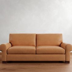 a tan leather couch sitting on top of a hard wood floor next to a white wall