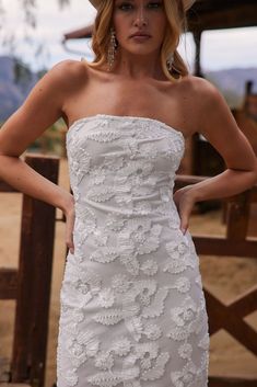 a woman in a white dress and hat posing for the camera with her hands on her hips