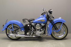 a blue motorcycle parked on top of a cement floor next to a gray wall in a room