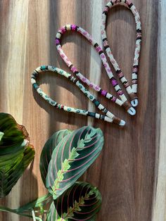 three necklaces on a wooden table next to a leaf and plant with the word love spelled in beads