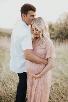 a pregnant couple cuddles in the tall grass