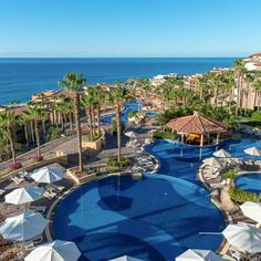 an outdoor swimming pool next to the ocean with umbrellas and palm trees around it