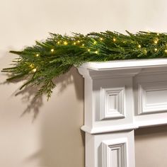 a christmas garland on top of a mantle with lights in the corner and evergreen branches