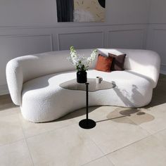 a white couch sitting on top of a tiled floor next to a vase with flowers