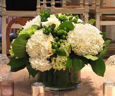 a vase filled with white flowers sitting on top of a wooden table next to candles