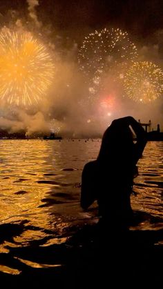 a person standing in the water watching fireworks