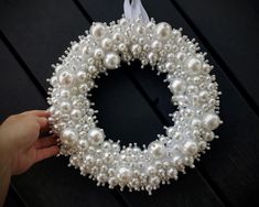 a hand is holding a wreath with white pearls and ribbon on the front of it