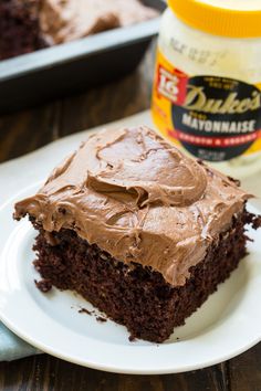 a piece of chocolate cake with frosting on a plate next to a container of peanut butter