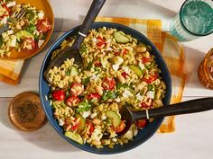 two bowls filled with pasta and vegetables on top of a wooden table next to utensils