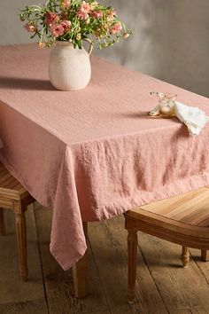 a pink table cloth with flowers in a white vase on it and two wooden chairs