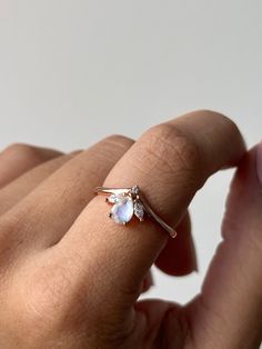 The Moonbeam Ring captures the serene beauty of the night sky, encapsulated in a stunning piece of jewelry. Featuring a pear-shaped moonstone at its heart, this ring reflects a soft, ethereal glow that changes with the light, evoking the tranquil radiance of moonlight. Accented by delicate marquise-cut stones on either side, the rose gold band adds a warm, luxurious touch, enhancing the moonstone’s natural brilliance. Whether you're seeking a unique ring, a meaningful gift, or a special addition Gold Moonstone Ring, Rose Gold Band, Unique Ring, The Night Sky, Moonstone Ring, Ring Size Guide, Marquise Cut, Earrings Collection, Gold Band