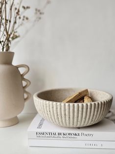 a white bowl sitting on top of a book next to a vase