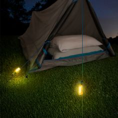 two lights are lit up in the grass next to a sleeping bag and tent at night