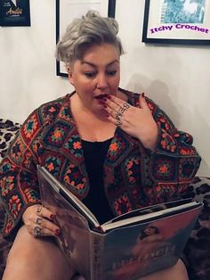 a woman reading a book while sitting on a couch with her legs crossed and finger in her mouth