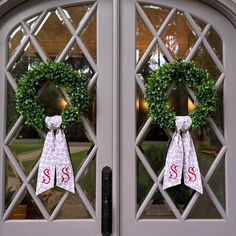 two wreaths with monogrammed bows hang on the front doors of a house