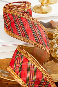 a red and green plaid ribbon on a wooden table next to a gold christmas tree