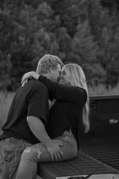 a man and woman are sitting on the back of a pickup truck with their arms around each other