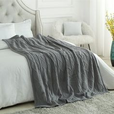 a white bed with a gray blanket on top of it next to a green vase