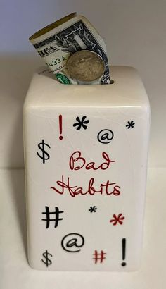 a money box with the words bad habitts written on it and a us one dollar bill sticking out of it