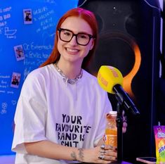 a woman with red hair and glasses sitting in front of a microphone holding a bottle