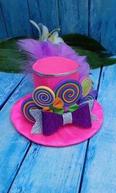 a pink top hat with purple and green decorations on the front, sitting on a blue wooden surface