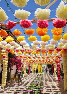 an outdoor walkway decorated with paper flowers and pom - poms in the sky