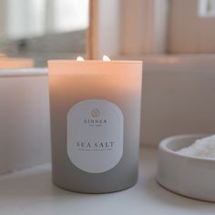 a lit candle sitting on top of a counter next to a bowl filled with sea salt