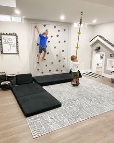 two children playing in a playroom with climbing walls and black sofas on the floor