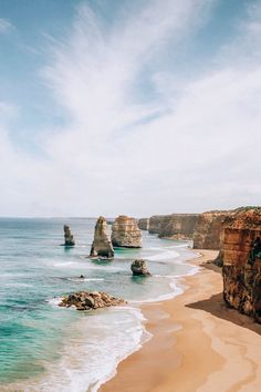 the beach is next to two large rocks in the water and there are waves crashing on it