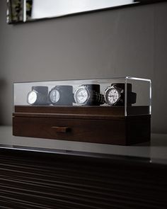 three watches sitting in a glass case on top of a wooden table next to a mirror