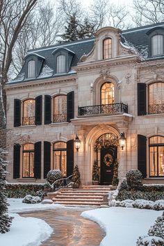 a large house with lots of windows and lights on it's front door in the snow