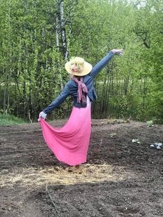 a woman in a long pink dress and cowboy hat standing on top of a dirt field