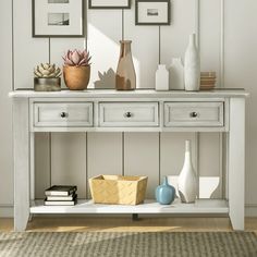 a white table with some vases and pictures on the wall next to it in a room