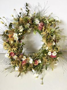 a wreath with flowers and greenery hanging on the wall next to a white wall