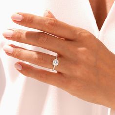 a woman's hand with a diamond ring on her left hand, wearing a white shirt