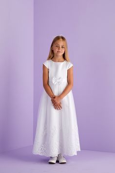 Ankle length first Holy Communion cap sleeve dress. A duchess satin dress with princess line detail, capped sleeves and front waistband with bow to centre front are complimented by the impressive scallop hem embroidery and sequin detail to the hem of the net tulle overlay skirt. Whilst at the back is a large pre tied bow with luxurious long tails completing the look and maintains a perfect bow each time you wear this dress. Fastened at the back with a hidden zip. This classic dress promotes pure Fitted Bow Dress For First Communion, Satin Fitted Dress For Confirmation, Fitted Satin Dress For Confirmation, Short Sleeve Dress With Fitted Bodice For Confirmation, Spring First Communion Dress With Short Sleeves, Fitted Dress With Bow For Confirmation, Princess Style First Communion Dress With Short Sleeves, Princess Style Short Sleeve First Communion Dress, Fitted Princess Style First Communion Dress With Short Sleeves