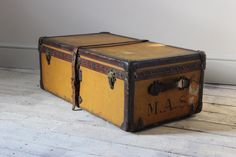 an old yellow suitcase sitting on the floor in front of a white wall and wooden floor