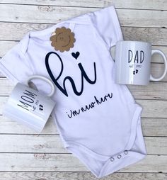 a baby bodysuit and coffee mug sitting on top of a wooden table next to it