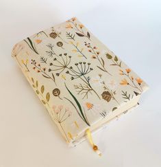 an open book with flowers on it sitting on a white table next to a yellow cord