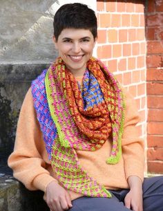 a smiling woman wearing a multicolored knitted scarf sitting on a stone step