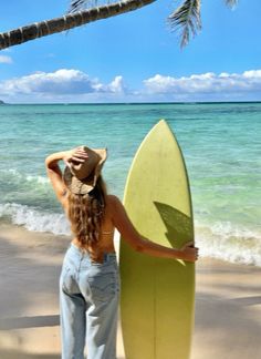 a woman holding a surfboard on top of a sandy beach next to the ocean