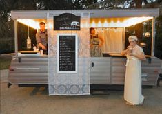 a woman standing in front of a food cart with a chalkboard sign on it