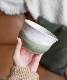 a person holding a white and green bowl in their hand on a brown leather couch