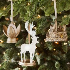 three ornaments hanging from a christmas tree in front of a lite - up castle