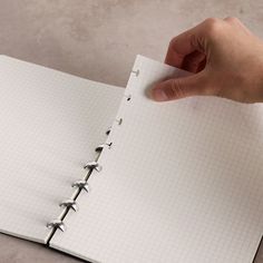 a hand holding a pen over a notebook with lined paper on it and an empty page in the middle