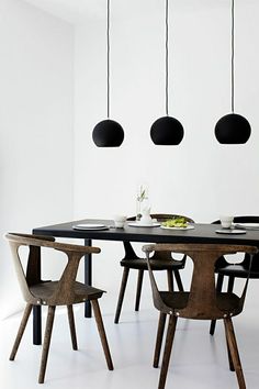 a table and chairs with black lamps hanging from the ceiling in front of white walls