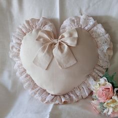 a heart shaped pillow with a bow on it next to a bouquet of pink roses