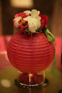 a red vase with white and red flowers in it sitting on top of a table