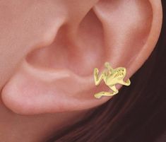 This gold Ear Cuff design comes in 2 variants: 1. 18k gold plated over Sterling Silver 2. 10k yellow gold   Our Gold Frog Ear Cuff climbs up the outer curve of your ear.  No piercing required.  Have fun wearing this playful jewelry! -*Ear Cuffs*- Ear Cuff earrings fit comfortably around the edge of your ear. They come in a variety of designs sure to catch attention and make you stand out. You can buy our cuffs as singlets or as a pair.  Ask if you have any questions. -*How It's Made*- These works are created through a multi-step process. We design, carve and modify waxes using the hands of our brilliant sculptors. The pieces are molded and cast with a personal touch. Every step of the way great care is taken to create only the best for you.  -*DIMENSIONS*- APPRX. LENGTH IN INCHES-1/2 APPRX Keroppi Cuff Earrings, Adjustable Gold Ear Climbers For Gift, Yellow Gold Clip-on Ear Cuff For Gift, Yellow Gold Clip-on Ear Cuff As Gift, Trendy Yellow Gold Ear Cuff As Gift, Trendy Yellow Gold Ear Cuff For Gift, Egirl Earrings, Gold Ear Cuffs, Wire Ear Cuffs