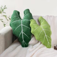 two green leaf pillows sitting on top of a white couch next to a book and plant